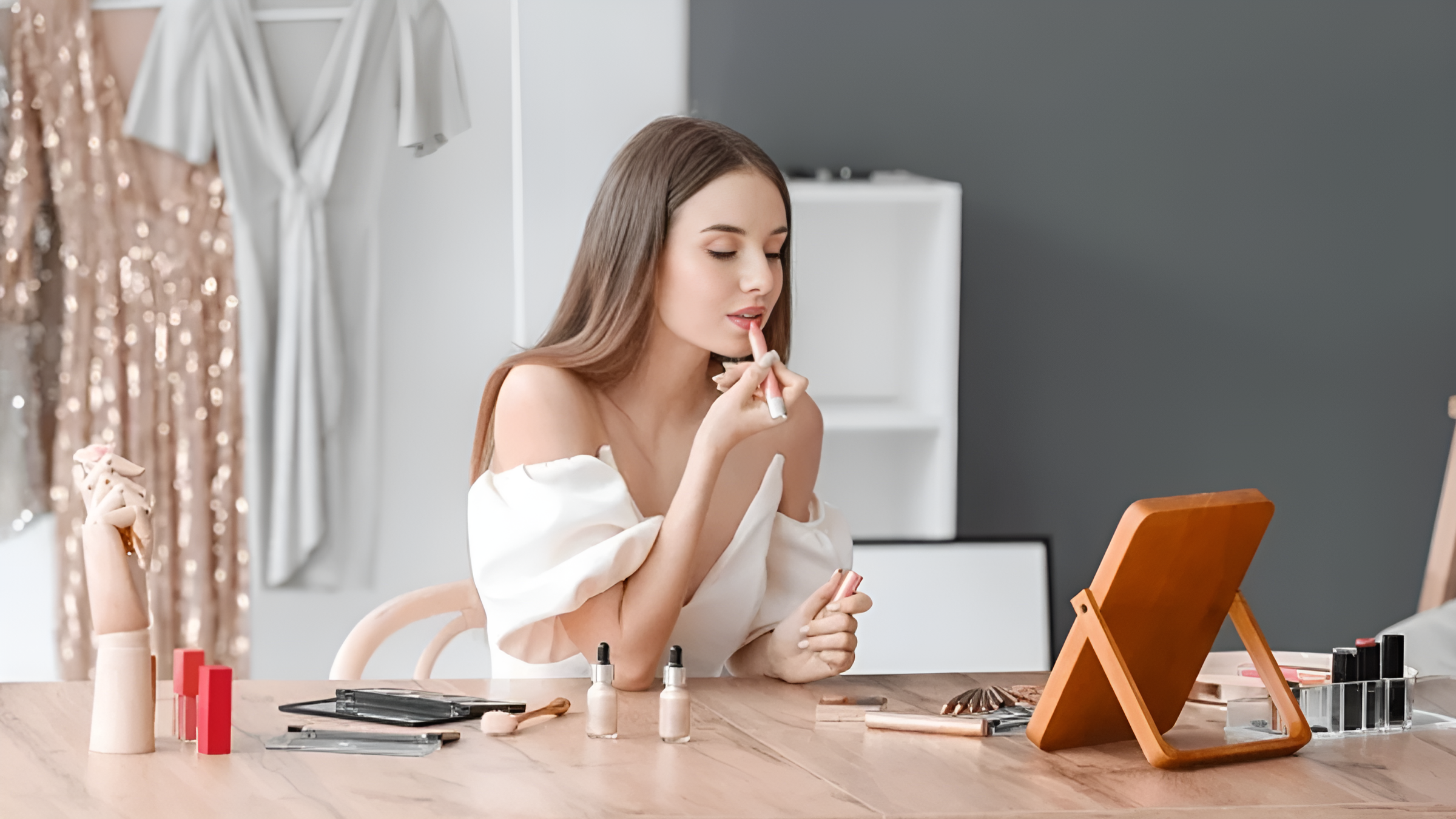 A young woman applying makeup in a bright vanity room with various makeup products on the table.